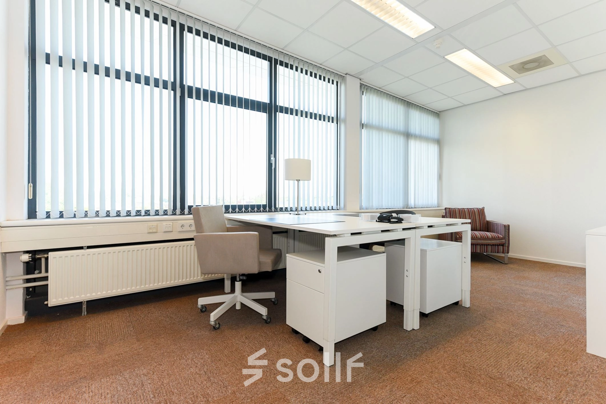 A well-lit, furnished office space for rent at Marshalllaan 2, Delft, featuring modern desks and chairs with large windows providing ample natural light.
