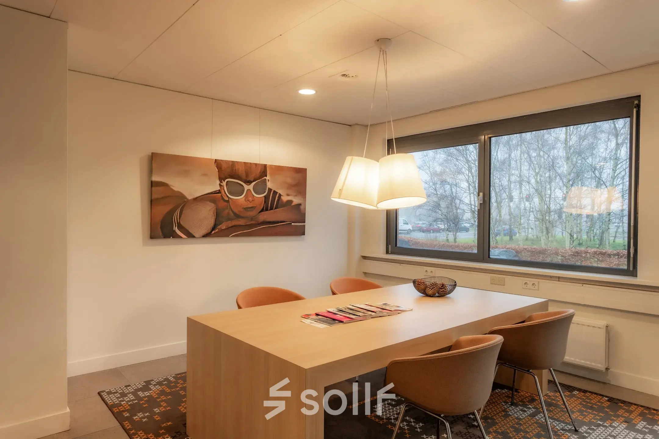 A furnished office space at Marshalllaan 2, Delft, featuring a wooden table, chairs, modern artwork on the wall, and large windows providing natural light. Ideal for office space rental.