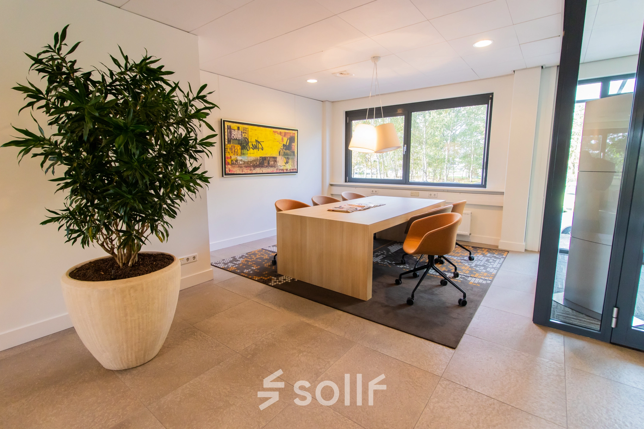 Bright office space at Marshalllaan 2, Delft, featuring a stylish meeting area with a large table, comfortable chairs, and a decorative plant. Perfect for anyone looking to rent office space.