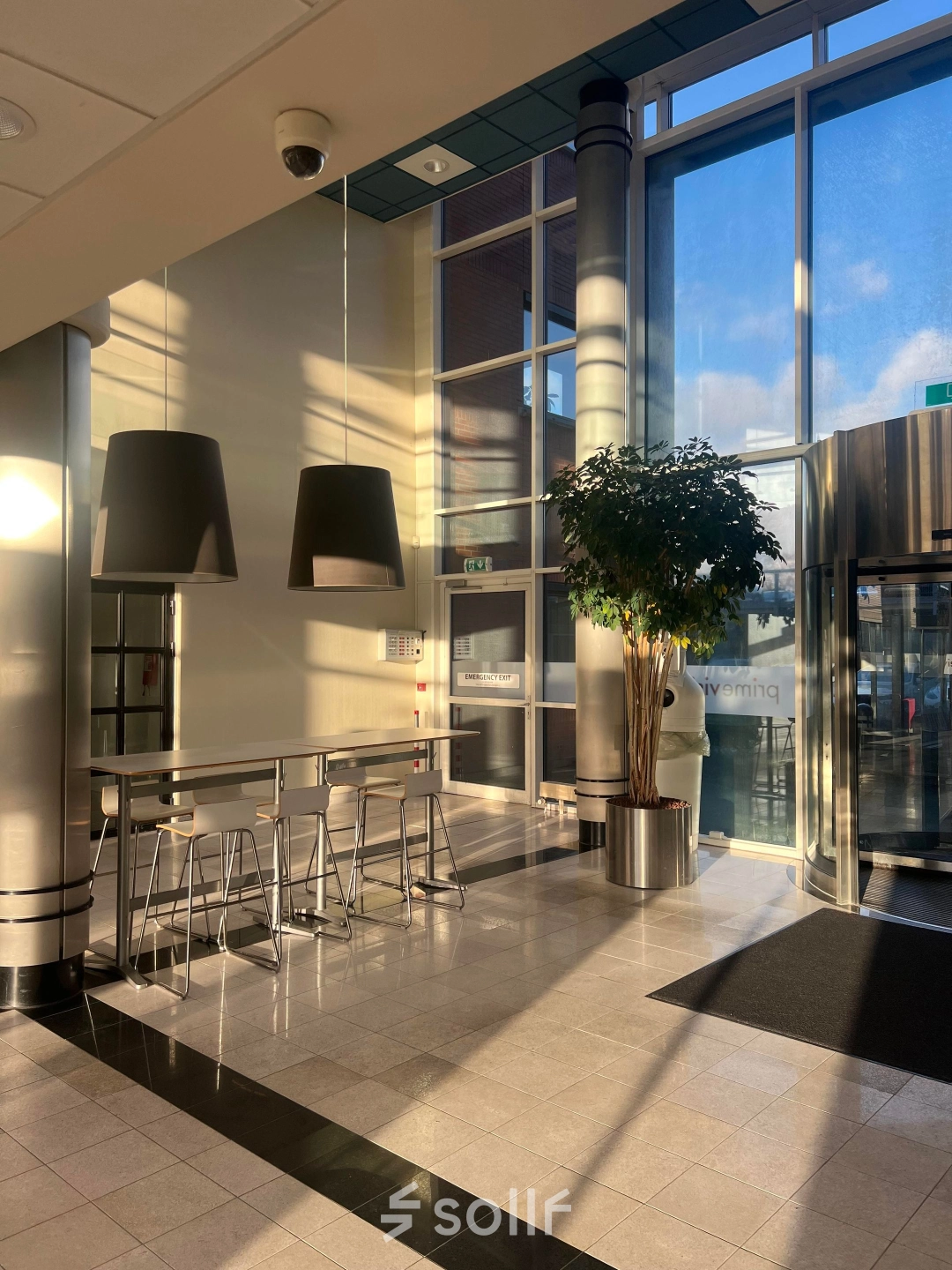 Bright lobby area with tall ceilings and modern lighting at an office to rent in Delft, featuring seating and large windows for natural light.