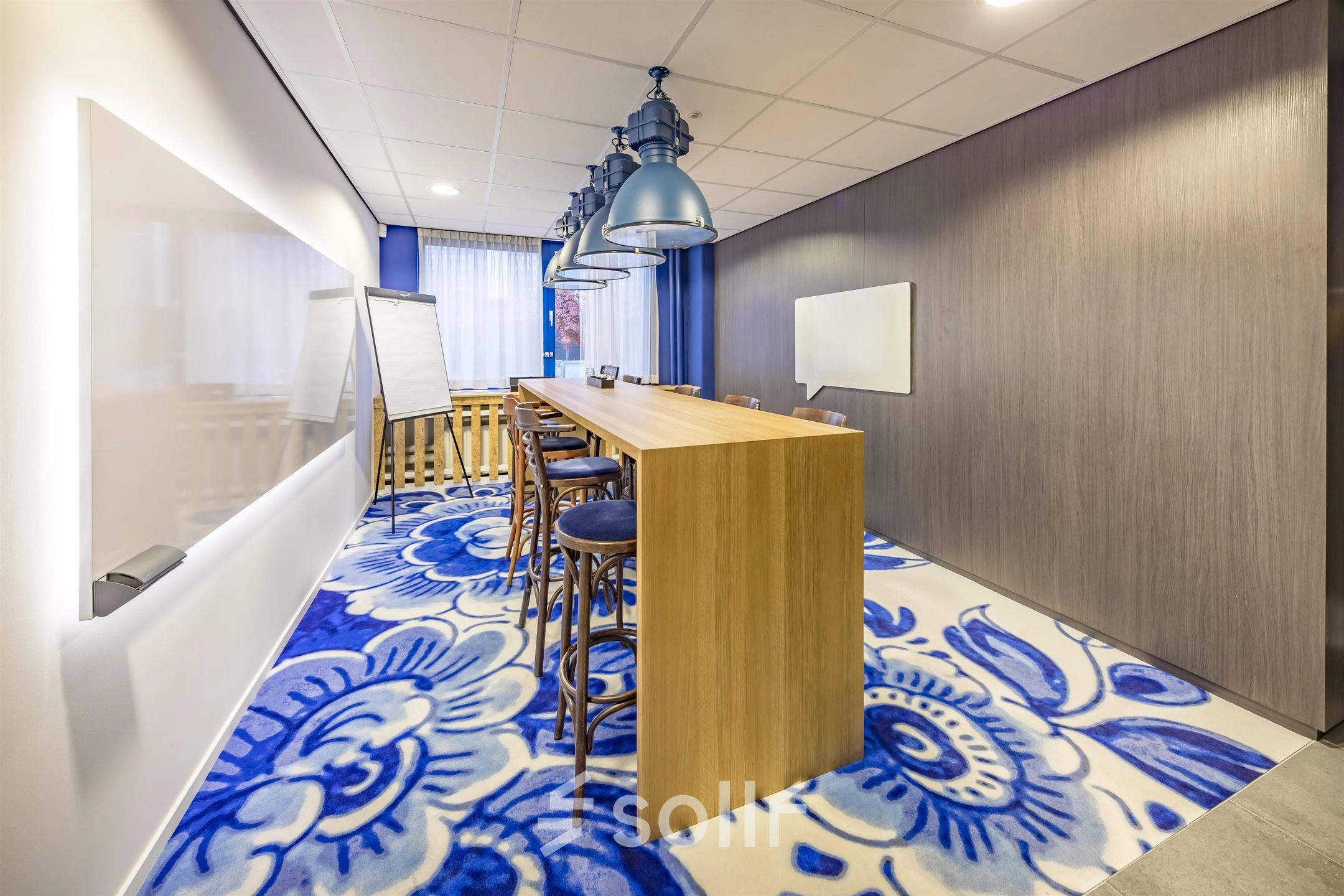 Brightly lit office space with a long wooden table and chairs on a floral carpet at Amerikastraat 3, Den Bosch, ideal for office space rental.