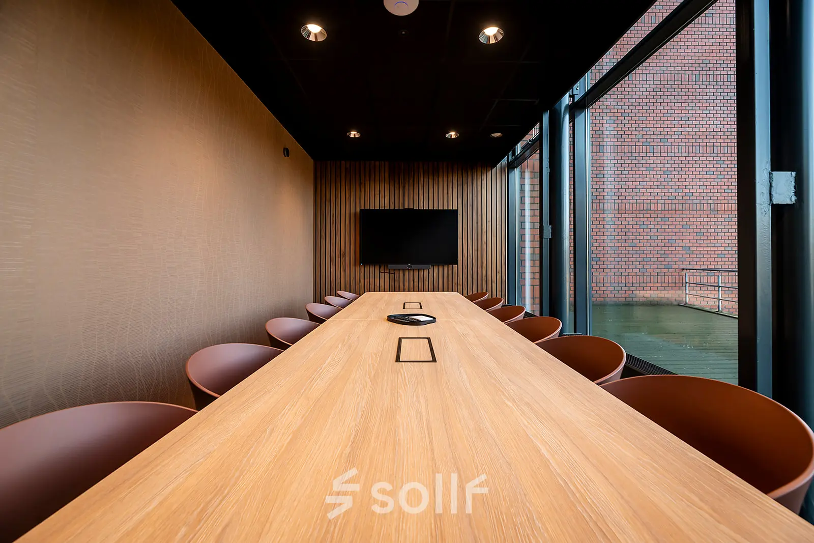 Modern conference room at Hambakenwetering 5 with a long wooden table, surrounded by chairs and a wall-mounted screen, ideal for office space rental in Den Bosch.