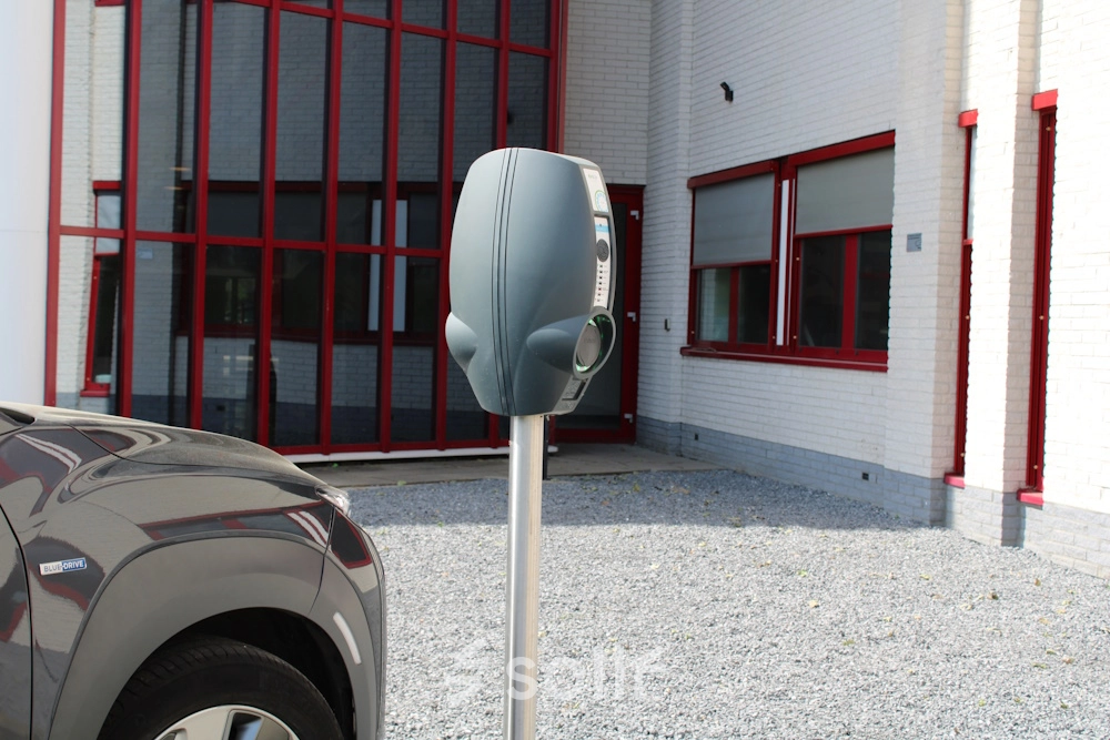 Exterior view of office space for rent at Keulenstraat 1, Deventer, featuring a parking area with an electric vehicle charging station.