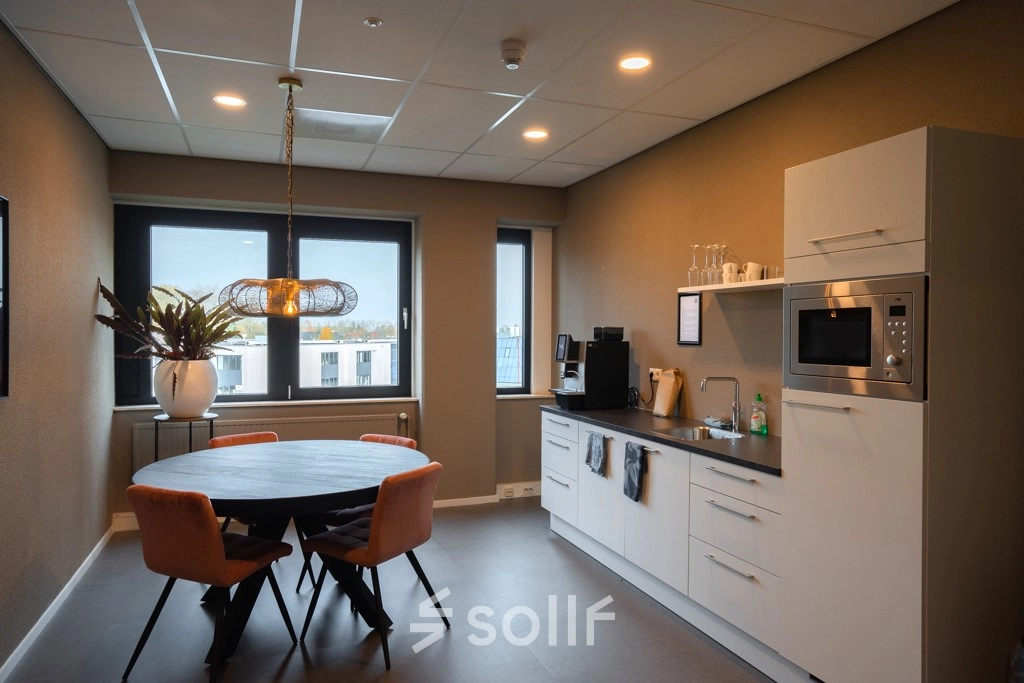 Modern office kitchen area at Keulenstraat 1, Deventer, available for office space rental, featuring a round table with chairs, microwave, and coffee machine.