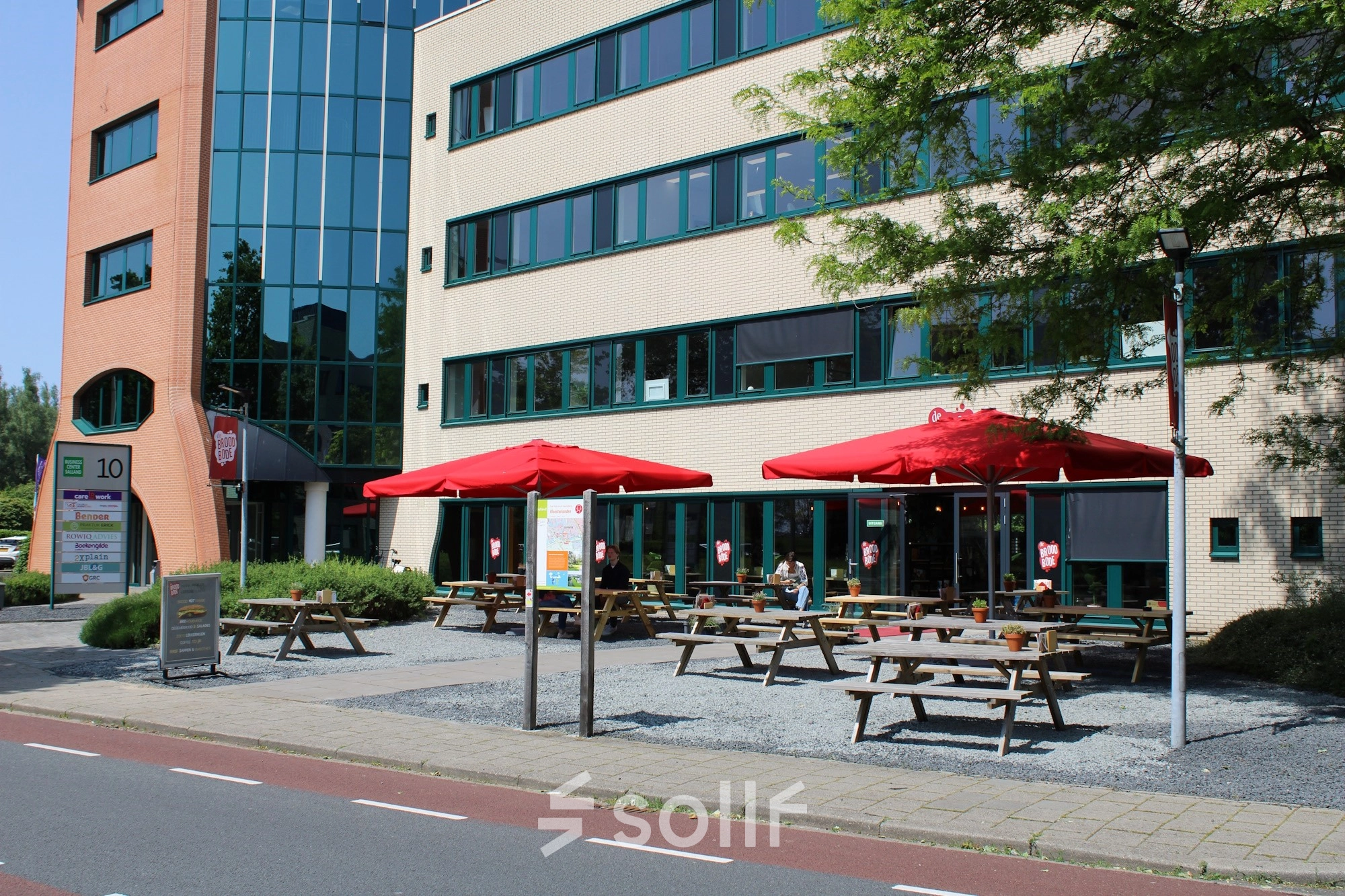 Exterior view of office space for rent at Keulenstraat 10, Deventer, featuring outdoor seating with red umbrellas.