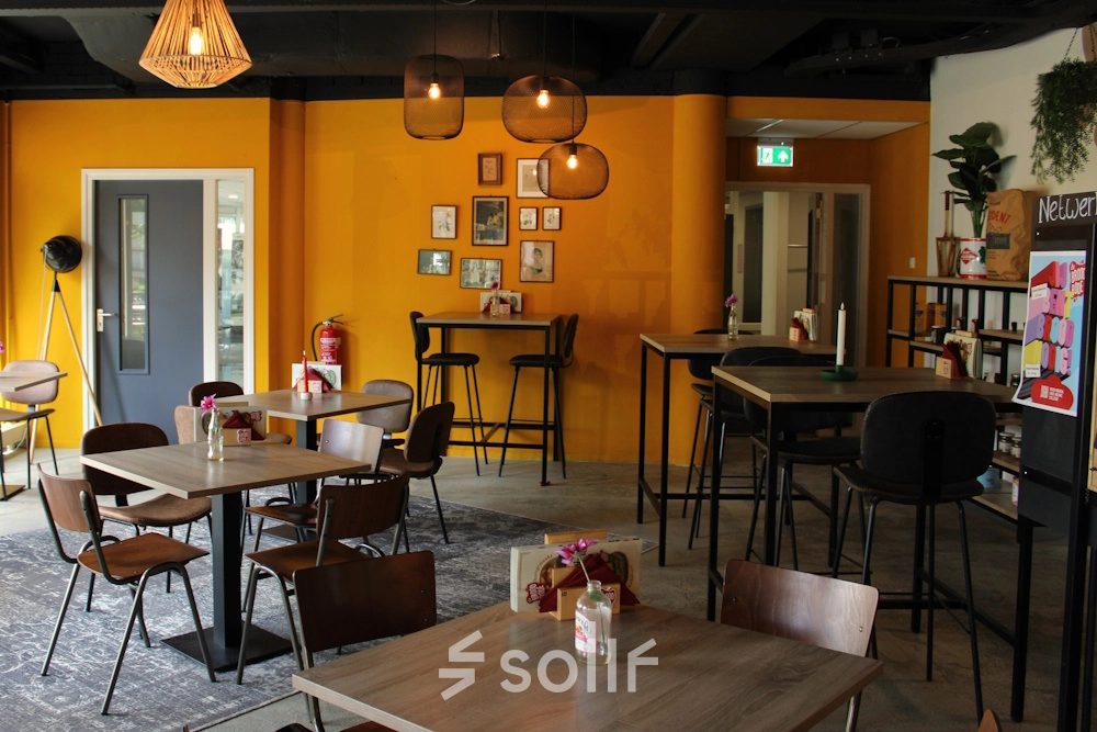 Lively office space for rent at Keulenstraat 10, Deventer, featuring modern furnishings with wooden tables and chairs, warm lighting, and wall decor. Ideal for office space rental.