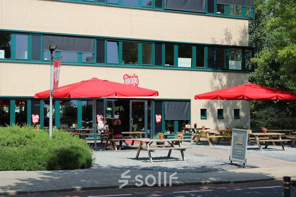 Exterior view of an office building at Keulenstraat 10, Deventer with outdoor seating under red umbrellas.