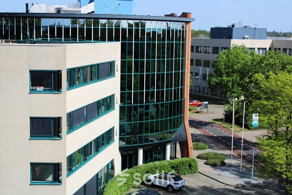 Exterior view of Keulenstraat 10 in Deventer, featuring a contemporary office building suitable for office space rental. The facade showcases large glass windows and a landscaped entrance area.