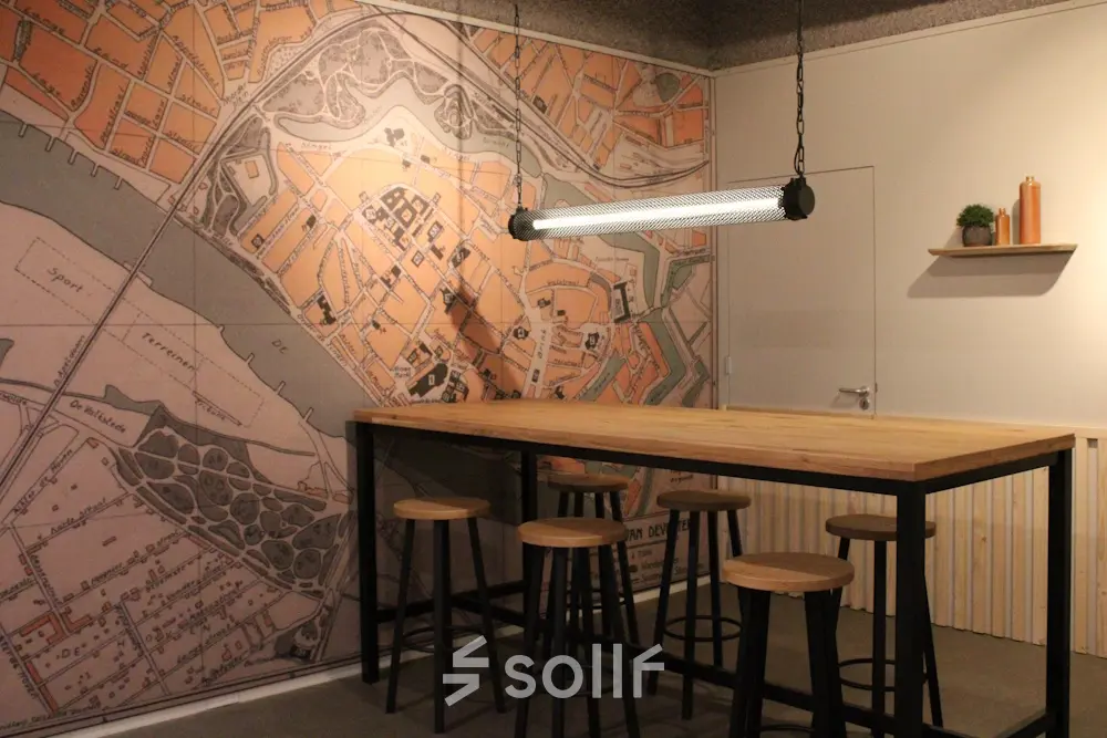 Modern office interior at Keulenstraat 12, Deventer featuring a large table, high stools, and a historic map mural. Ideal for those seeking office space rental with character.