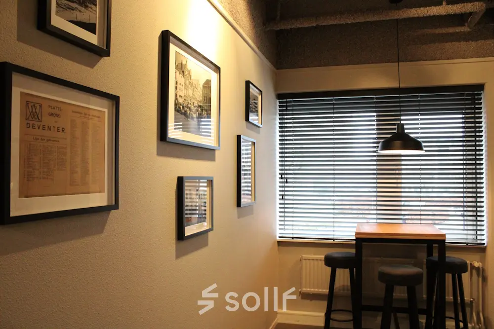 Cozy corner office space at Keulenstraat 12 in Deventer featuring a high table with stools and wall decor, perfect for casual meetings. Ideal for office space rental needs.