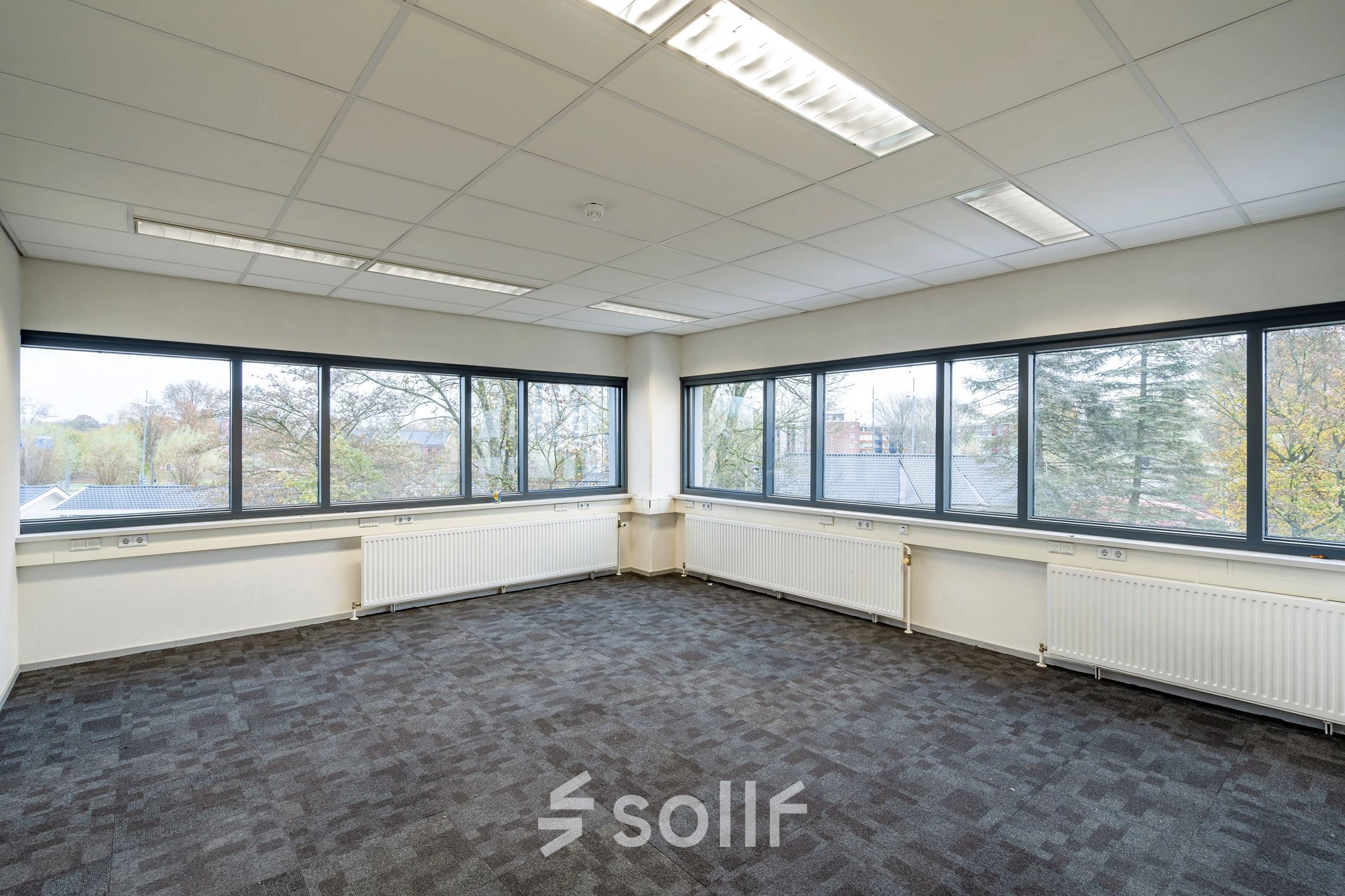 Bright office space available for rent at Staverenstraat 15-17, Deventer, featuring large windows and carpeted floors.