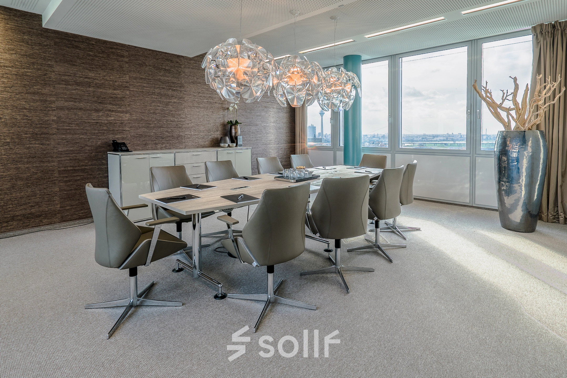 Spacious conference room for office space rental at Dreischeibenhaus, Düsseldorf. It features modern chairs, a large table, and decorative lighting with a city view.
