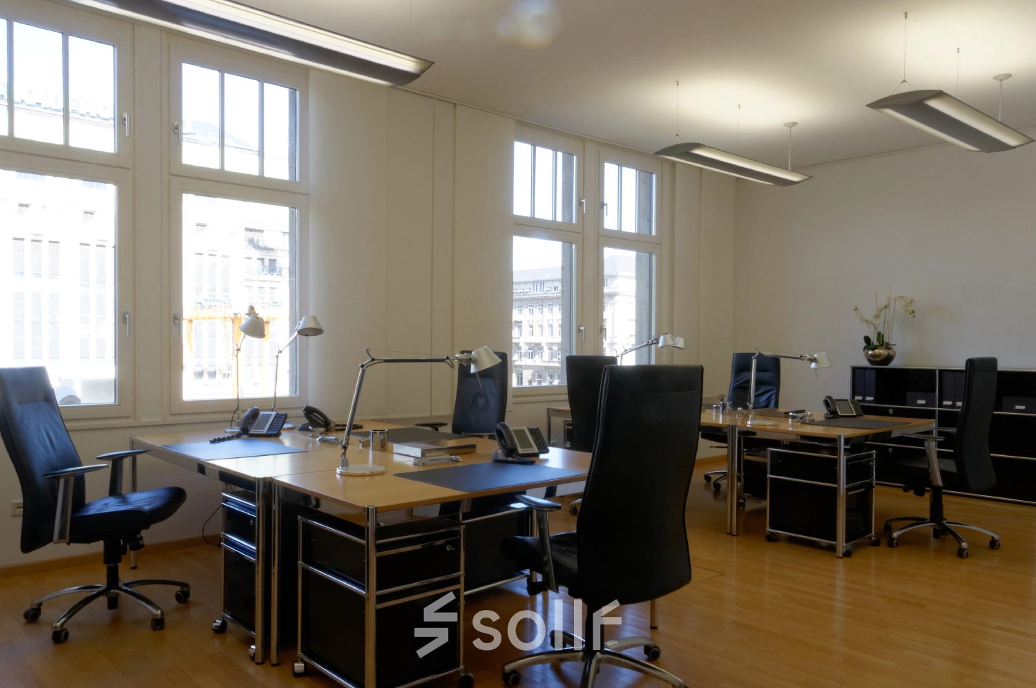A furnished office to rent at Königsallee 14, Düsseldorf Old Town, featuring multiple desks, chairs, and ample natural light through large windows.