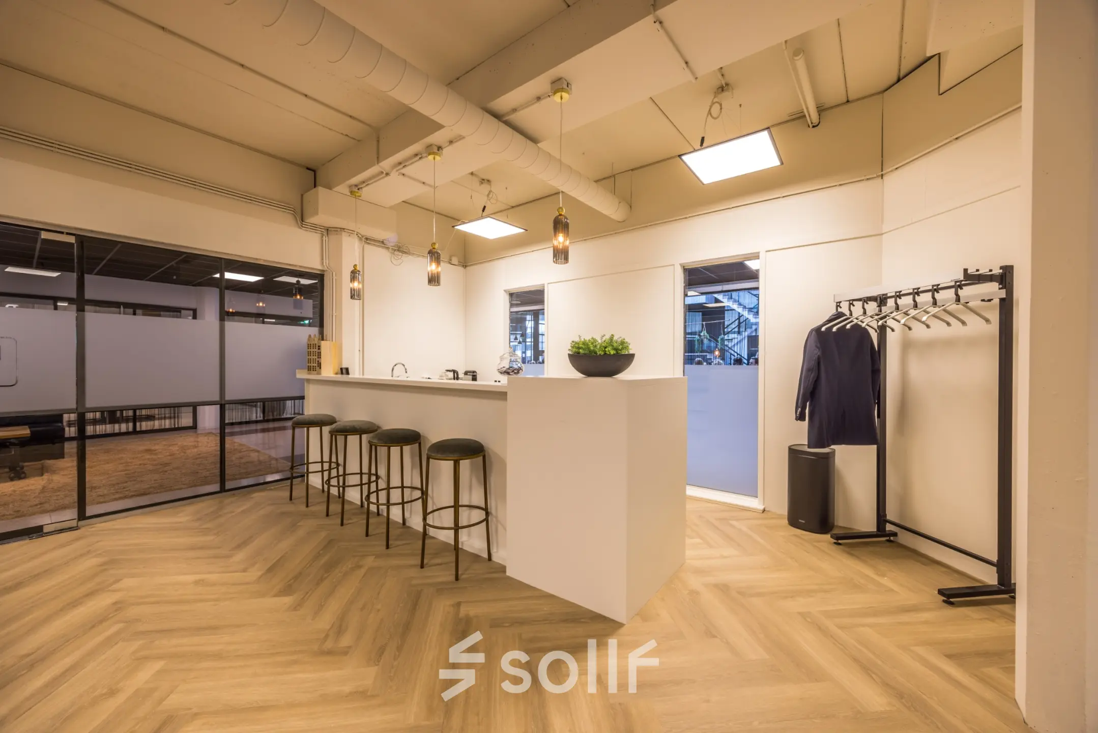 Stylish office space for rent at Luchthavenweg 81, Eindhoven Airport featuring a modern bar area with stools, warm lighting, and a nearby coat rack.
