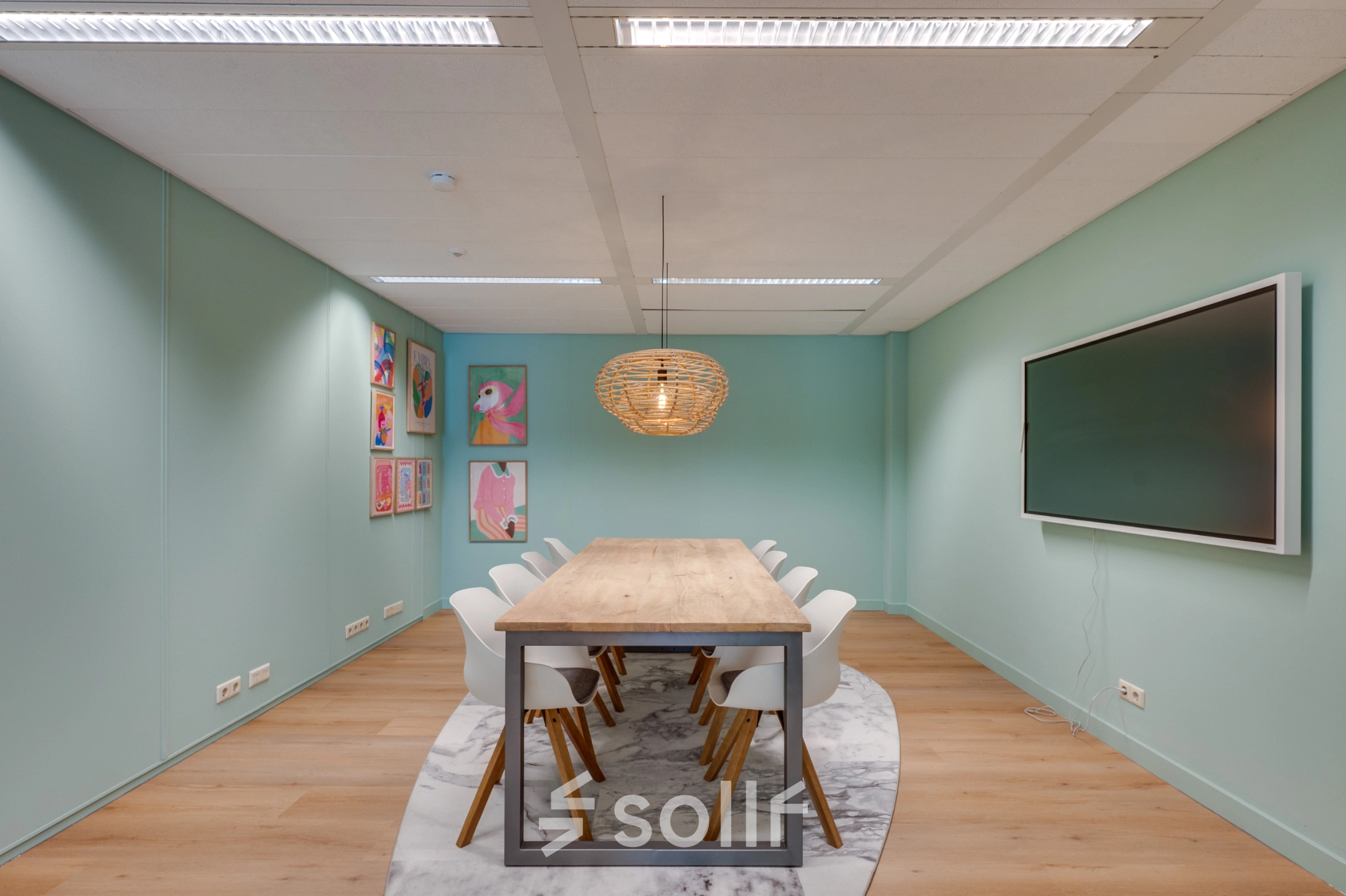 Furnished office space for rent in Eindhoven Center featuring a long table with chairs, wall-mounted screen, and decorative art pieces.