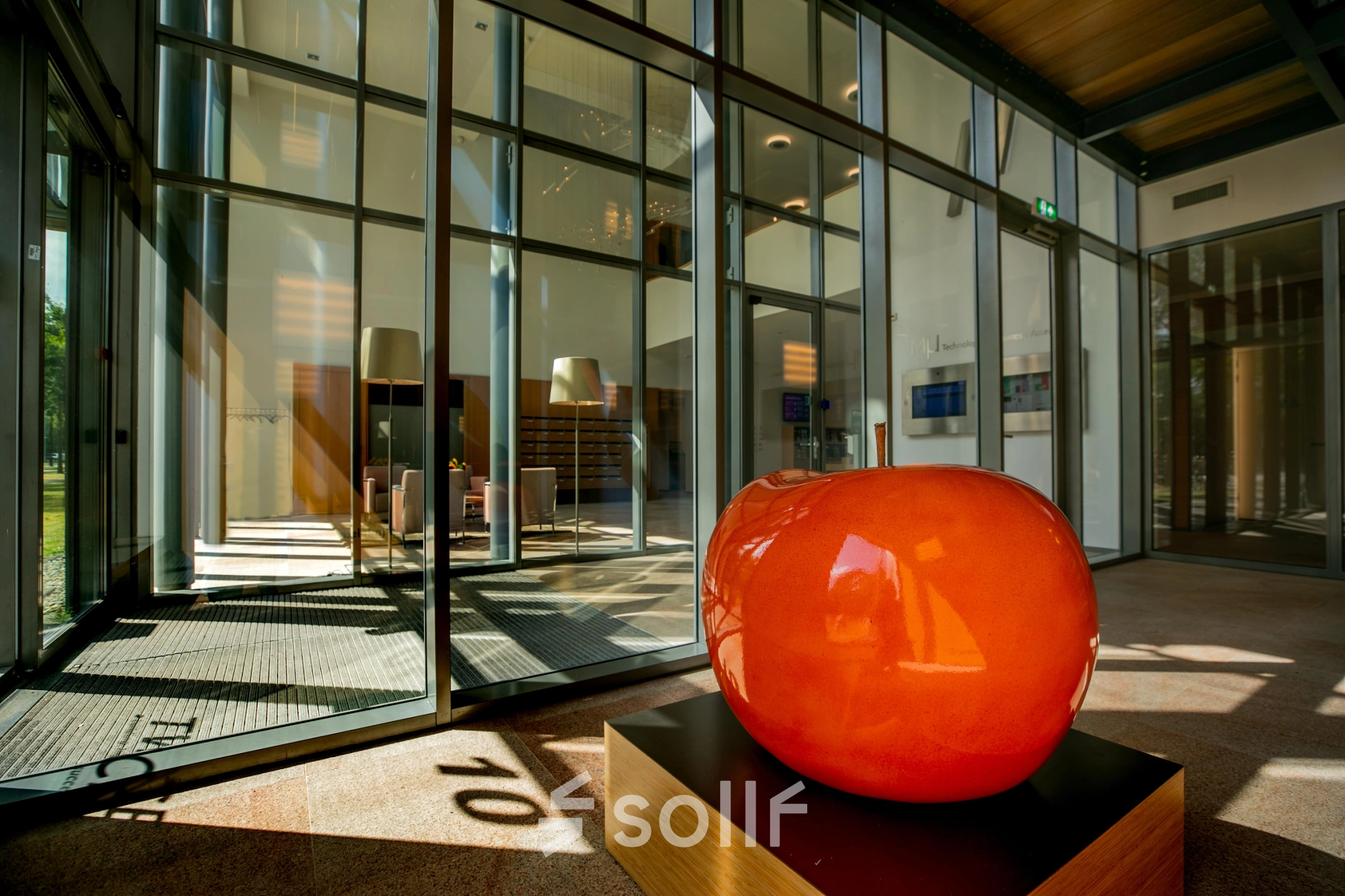Modern office entrance at High Tech Campus 10, Eindhoven with large glass panels and vibrant orange sculpture, ideal for office space rental.
