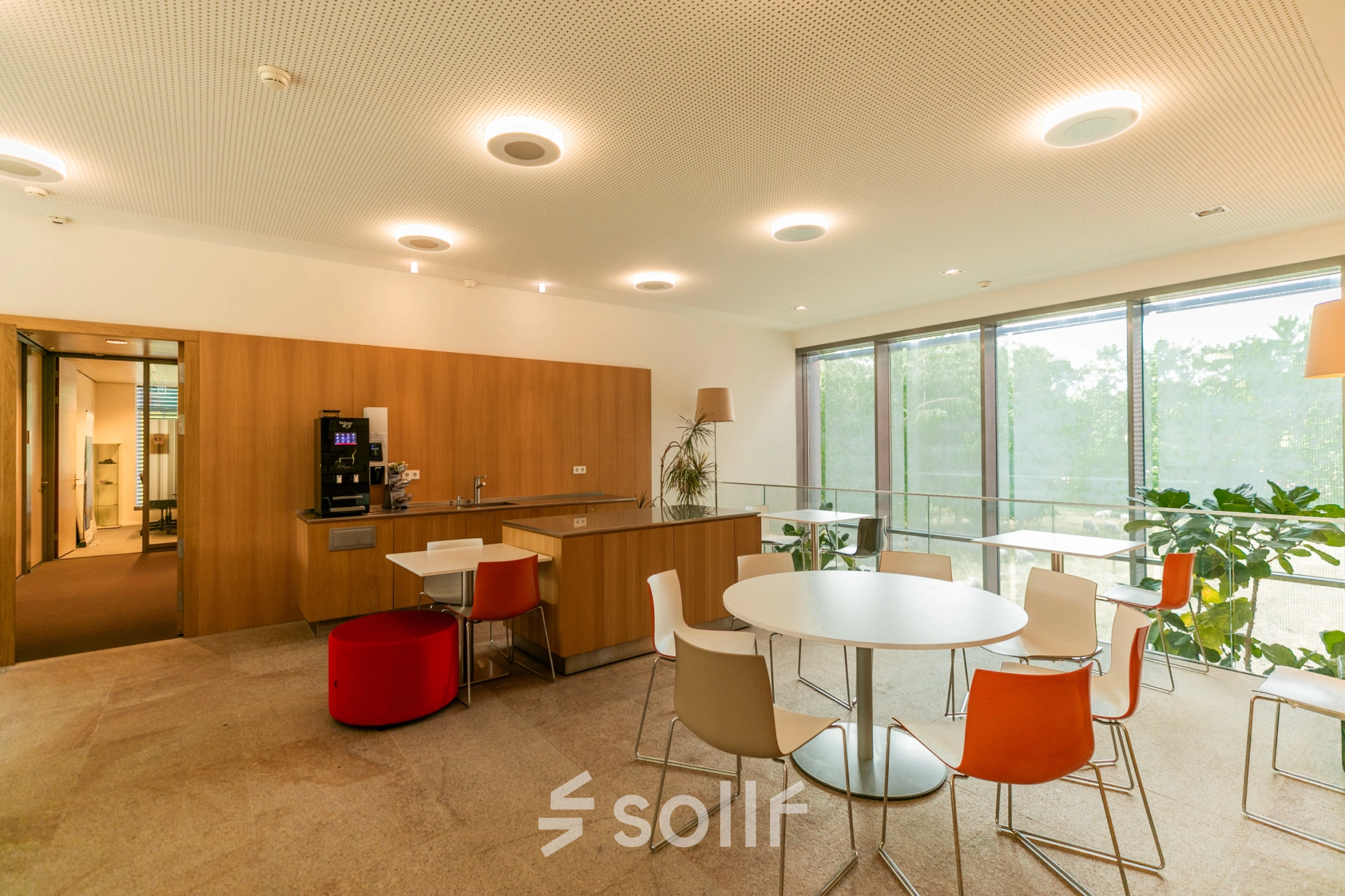 Modern office space rental at High Tech Campus 10, Eindhoven, featuring a bright, open lounge area with tables, chairs, and a coffee machine, perfect for informal meetings or a quick break.