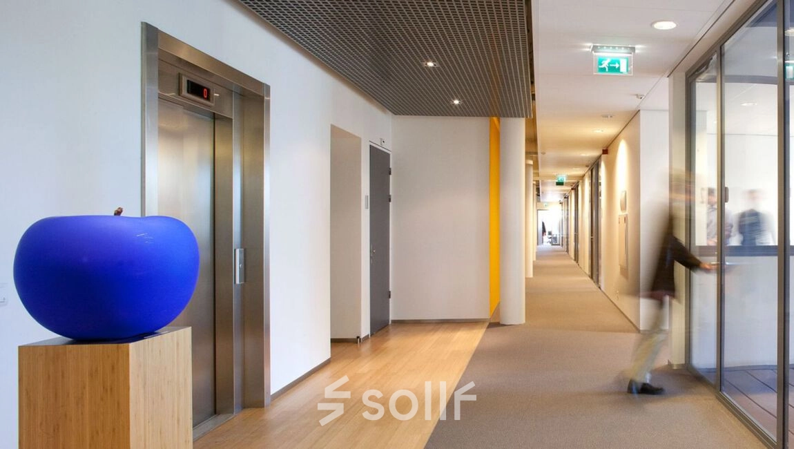Modern hallway at High Tech Campus 9, Eindhoven, featuring sleek decor and efficient layout. Ideal for office space rental, combining functionality with a clean design. A person walks down the corridor, adding dynamic movement.
