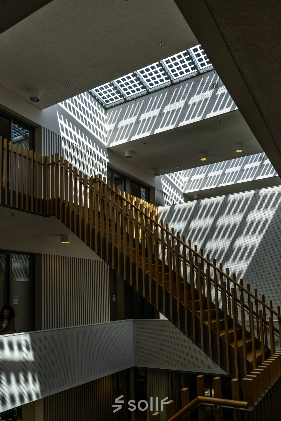 Interior view of a modern office space at TU campus, De Lismortel 31, Eindhoven High Tech Campus. Featuring geometric shadows and a wooden staircase, ideal for office space rental.