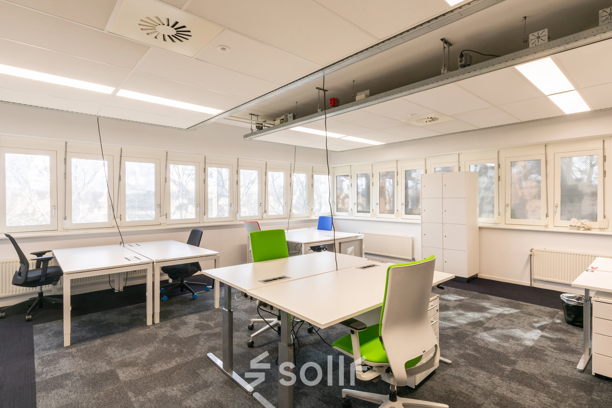 Modern office space rental at TU campus, Eindhoven High Tech Campus, featuring spacious work desks and ergonomic chairs in a bright, window-lined room.
