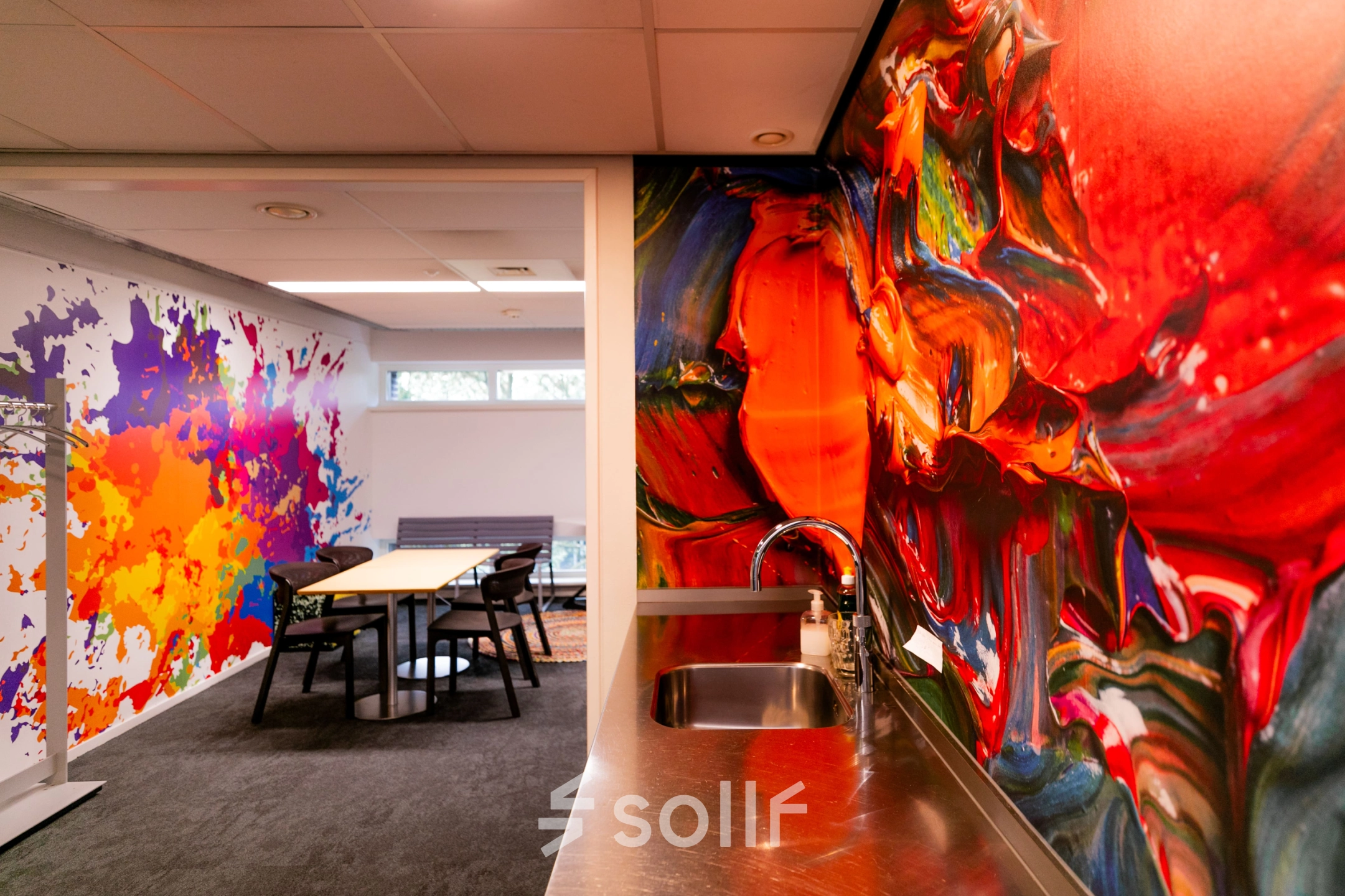 Vibrant interior at TU Campus, De Zaale 11 in Eindhoven, featuring colorful walls and a meeting area, ideal for office space rental. Includes a small kitchenette with a stainless steel counter and sink.