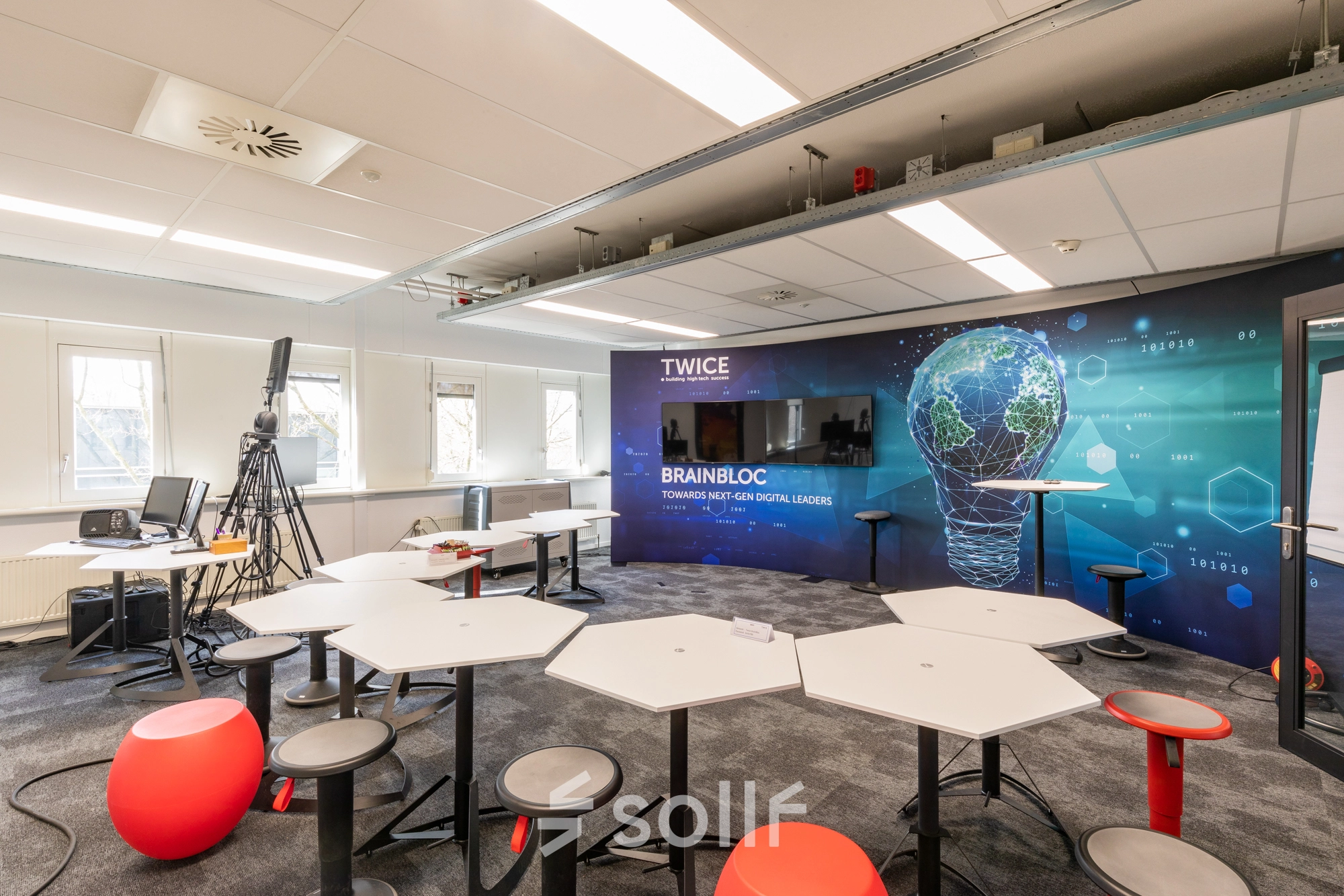 Modern office space at TU campus, De Zaale 11, Eindhoven High Tech Campus, featuring innovative workspaces with unique hexagonal desks and a digital-themed wall, ideal for office space rental.
