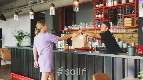 Two people interact at a modern bar area within an office at Torenallee 20, Eindhoven Strijp-S, showcasing opportunities for office space rental.
