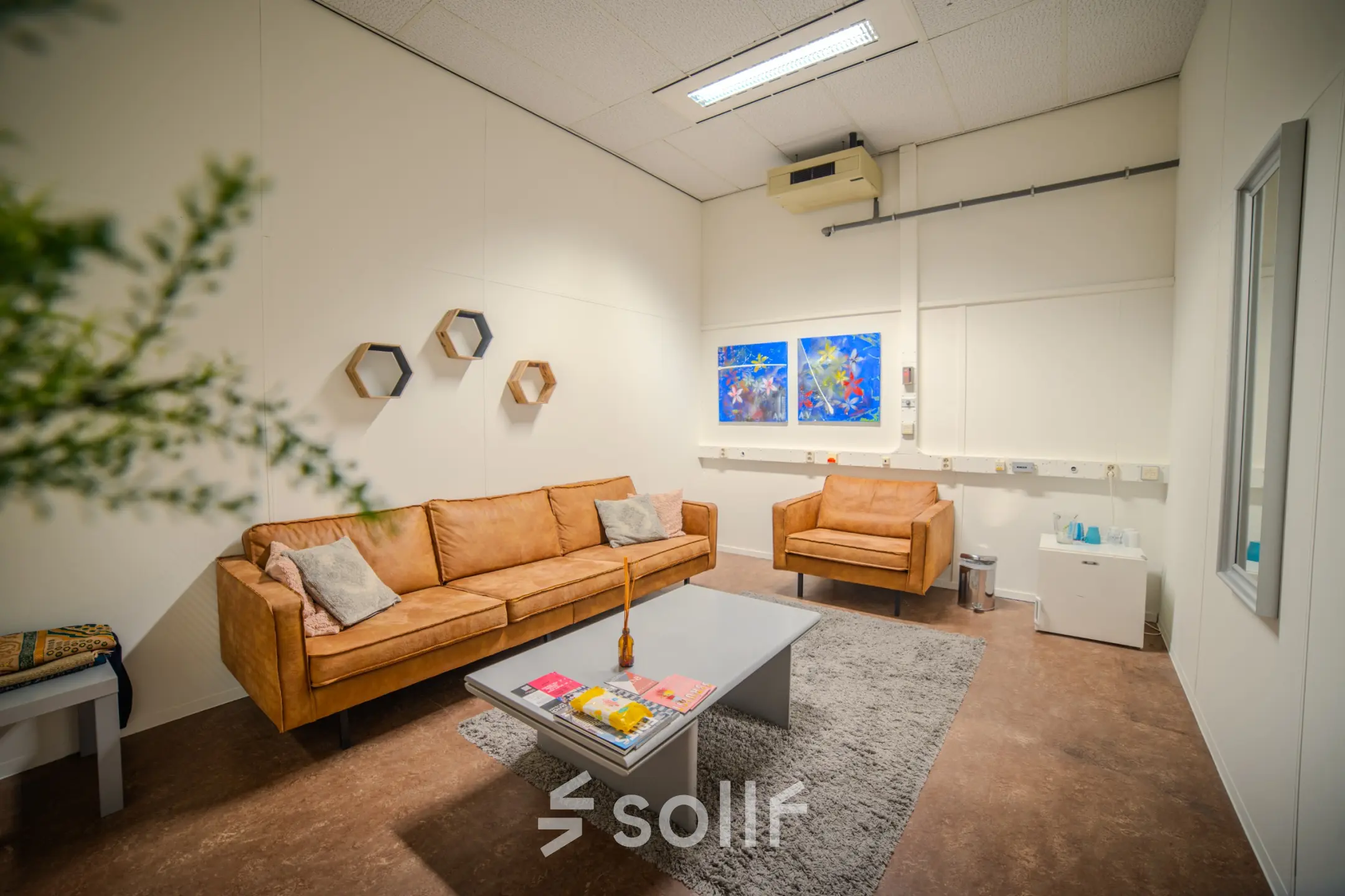Furnished office lounge at Torenallee 20, Eindhoven Strijp-S, featuring comfortable seating, a coffee table, and wall art. Ideal office space rental.
