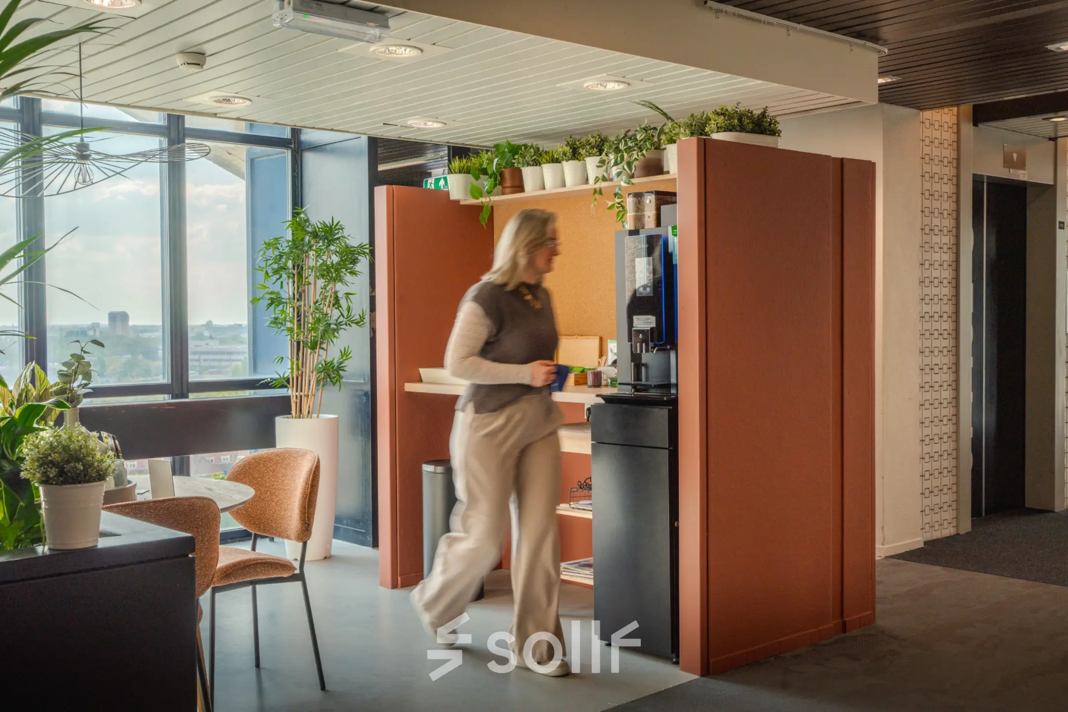 Modern office space at Torenallee 20, Eindhoven Strijp-S with a cozy seating area, coffee station, and plants. Office to rent offers stylish environment.