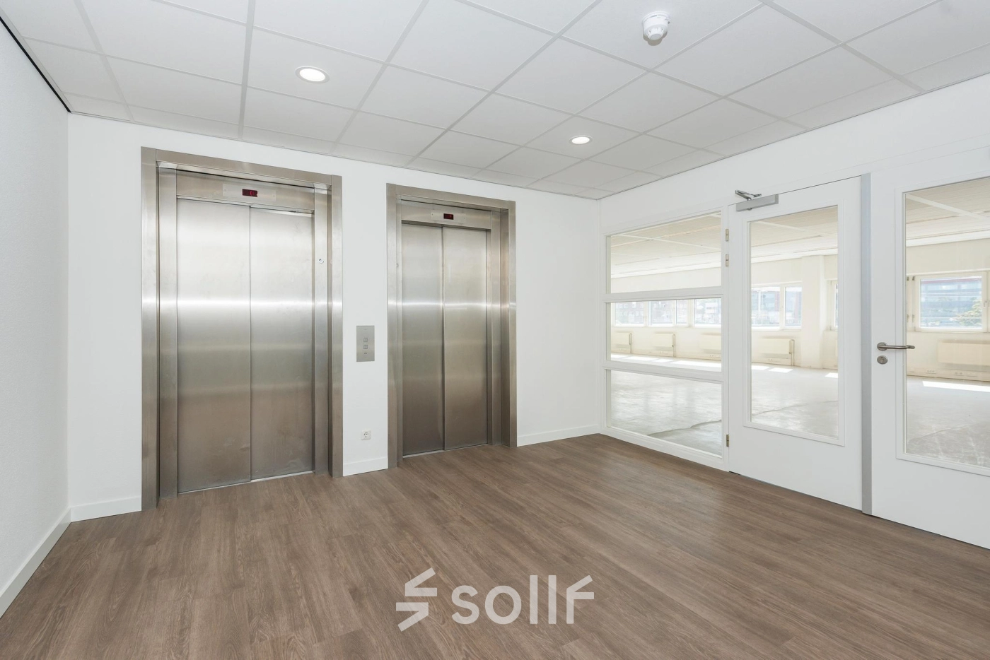 Interior view of office building at Brandweerstraat 20-30, Enschede featuring modern wood flooring and two sleek elevators, ideal for office space rental.