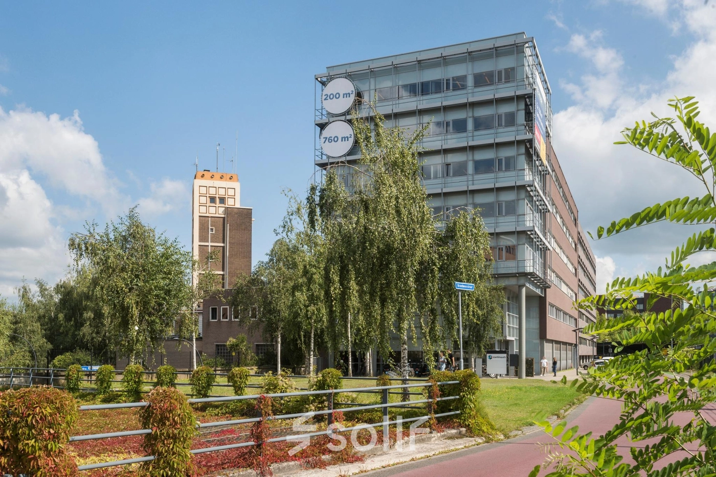 Exterior view of the office building at Brandweerstraat 20-30, Enschede, showcasing modern architecture with large windows. Ideal for office space rental, surrounded by greenery and a bike path in front.