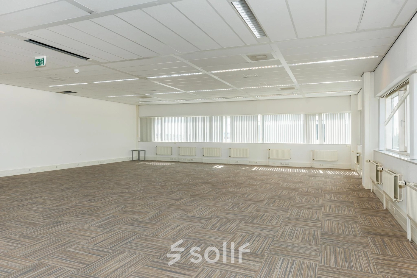 Spacious unfurnished office interior with neutral carpet and large windows, suitable for office space rental at Brandweerstraat 20-30, Enschede. Abundant natural light enhances the open, professional environment.