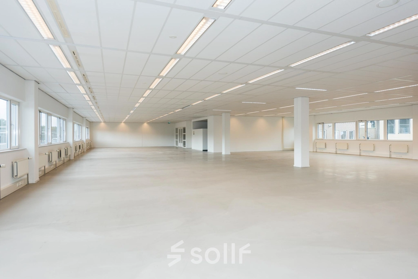 Spacious open floor plan with abundant natural light at Brandweerstraat 20-30, ideal for office space rental in Enschede. Minimalist design with ceiling lights and large windows.