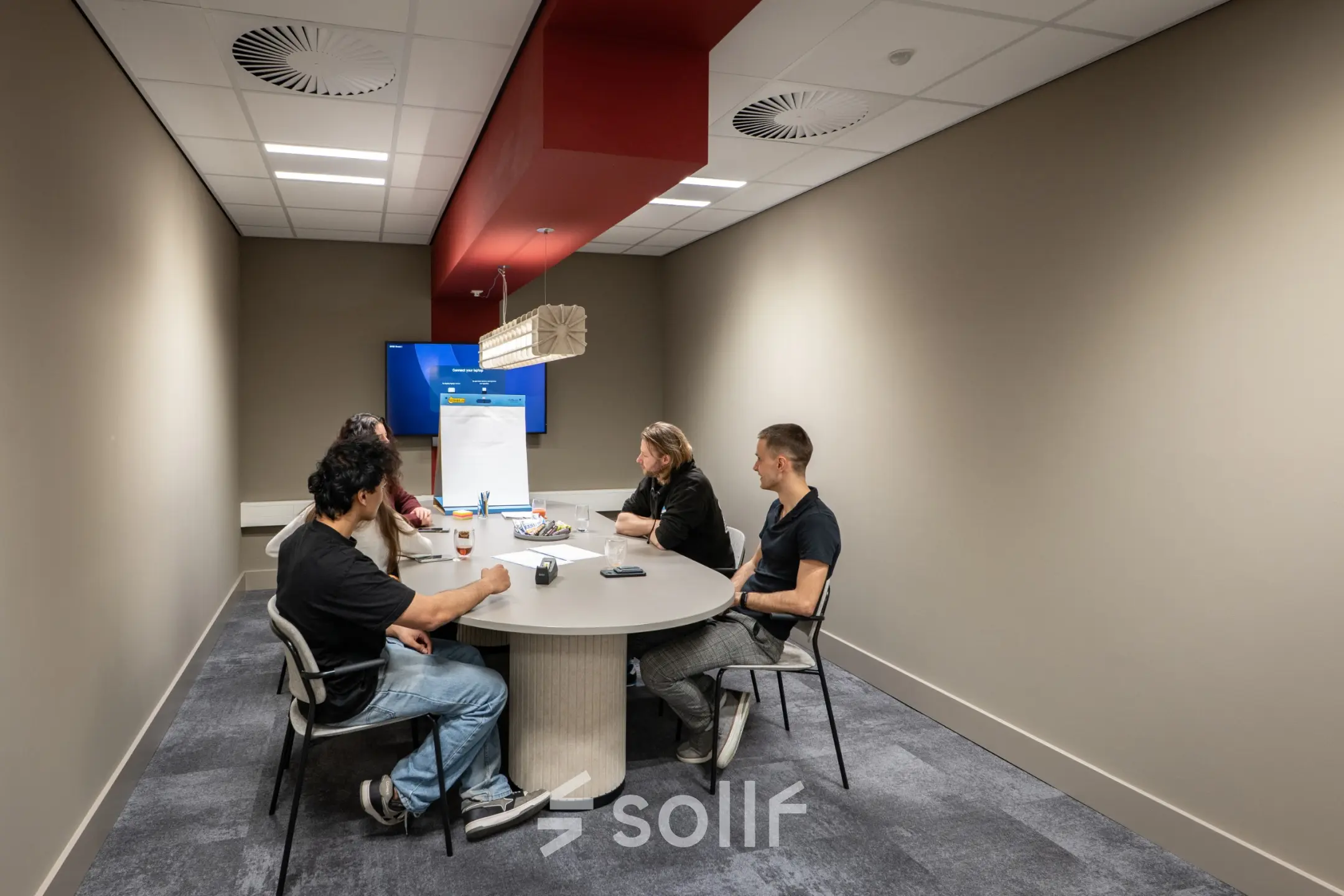 Four people engage in a meeting around a table in a modern office space in Enschede, ideal for office space rental.