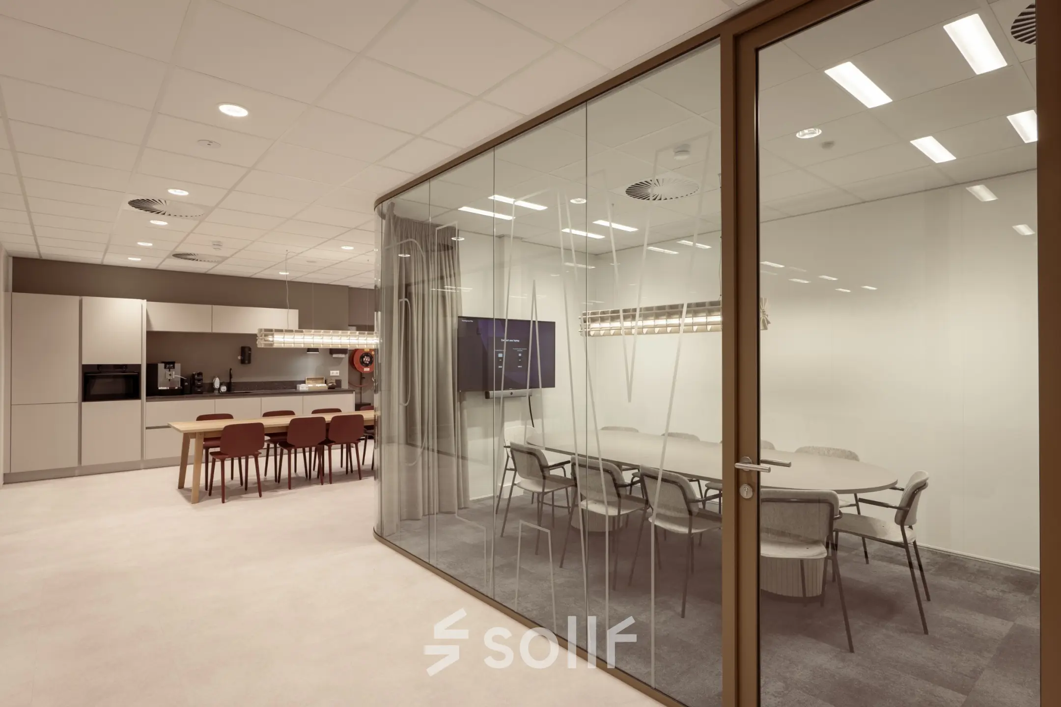 Modern office space available for rent in Enschede, featuring a conference room with glass walls and a furnished common area including tables and chairs.