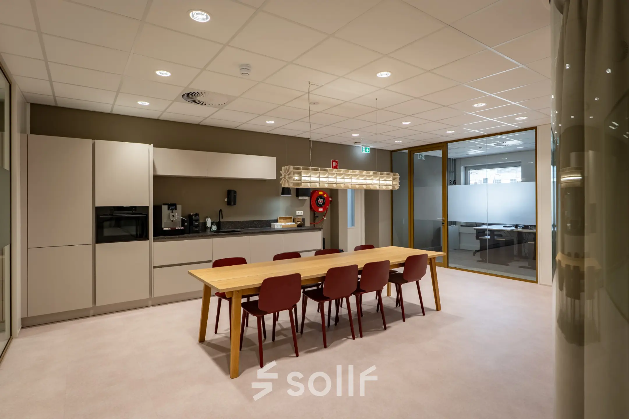 Furnished office interior at Kuipersdijk 2-4, Enschede, featuring a wooden table with red chairs and a kitchenette, ideal for office space rental.