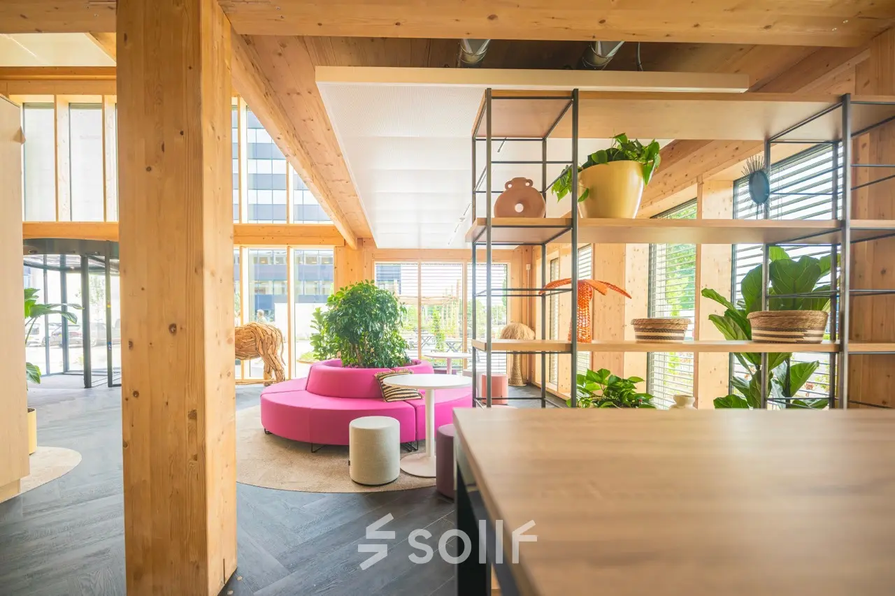 Bright, modern office space at Moutlaan 1-23, Enschede with wooden beams, vibrant seating, and open shelving. Ideal office space rental for dynamic work settings.