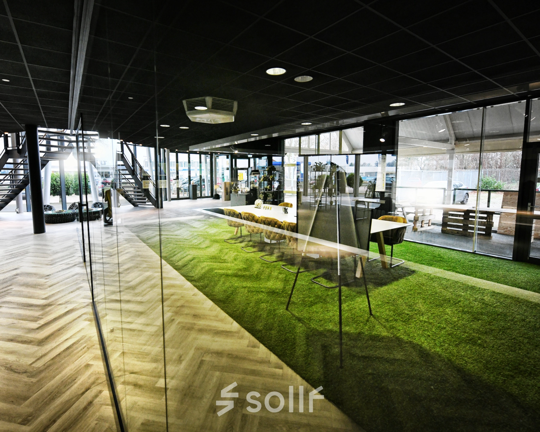 Spacious and modern office space with large windows and green flooring. Ideal for office space rental at Parkweg 102, Enschede. Features a meeting area and sleek design.