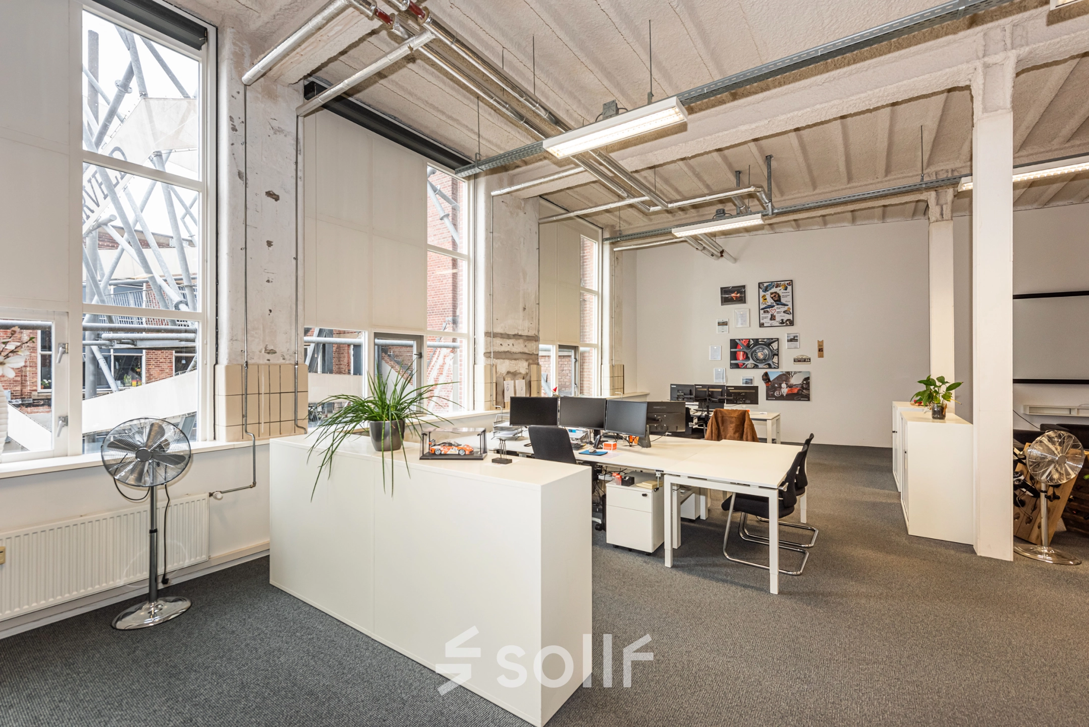 An office space with several workstations, potted plants, and large windows at Rigtersbleek-Zandvoort 10 in Enschede, available for rent.