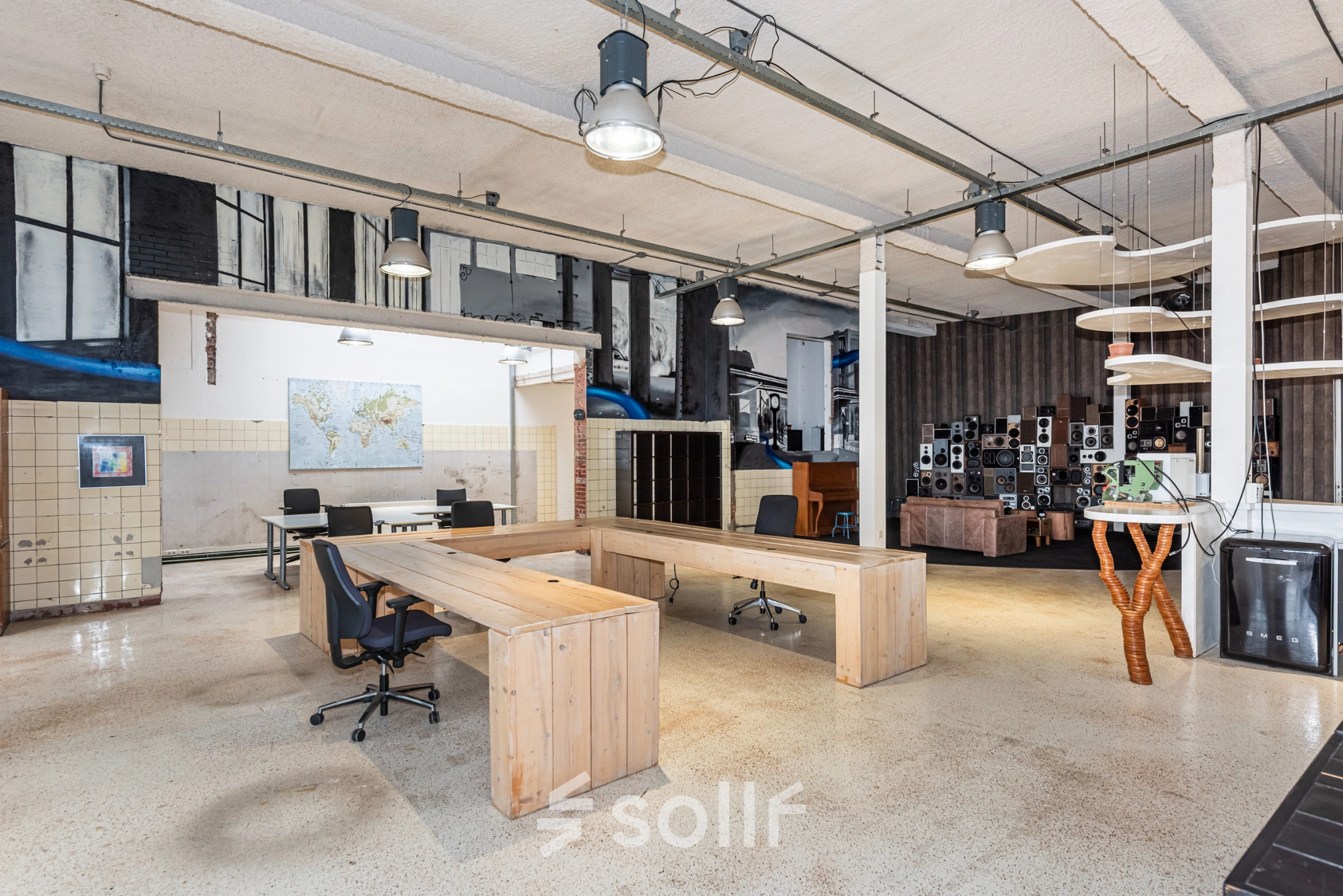 A spacious office with industrial decor and wooden desks arranged for workspace use. The office location is available for rent in Enschede.