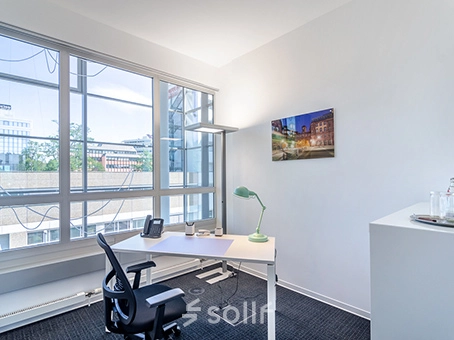 Bright office space at Mergenthaler Allee 15-21 in Eschborn with a desk and chair near large windows, ideal for office space rental.