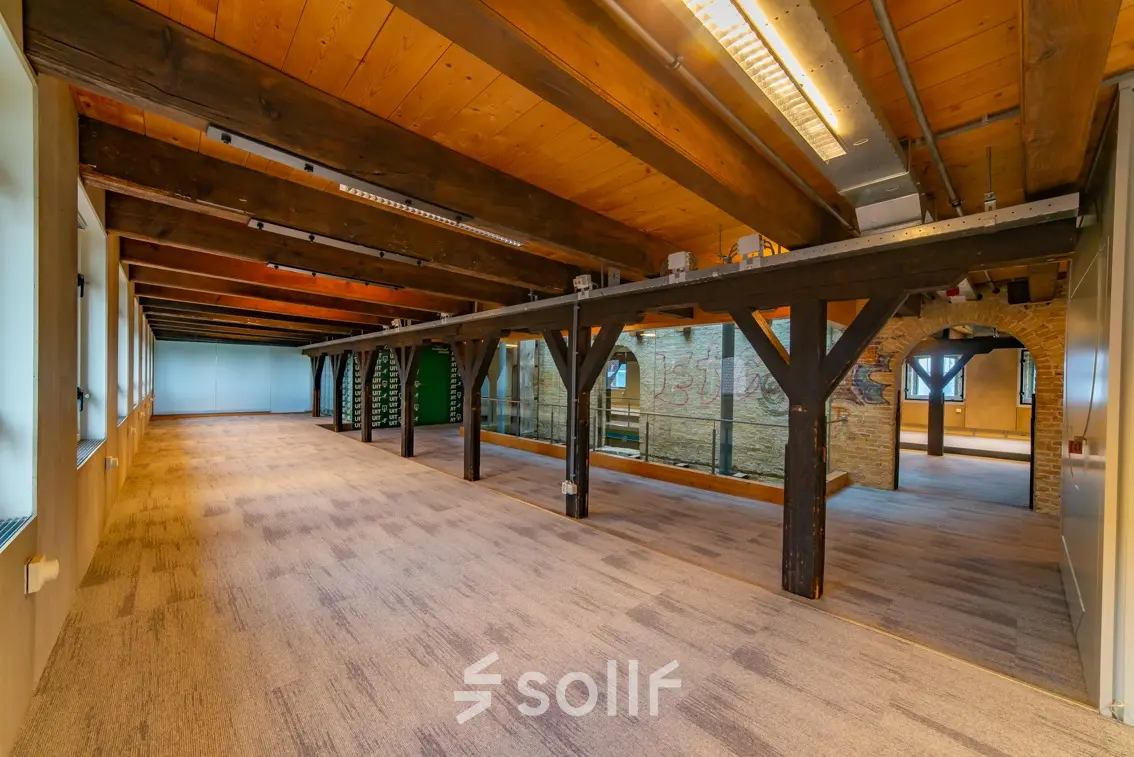 Spacious open office space with wooden beams and carpeted flooring at Prins Hendrikkade 3, ideal for office space rental in Franeker.