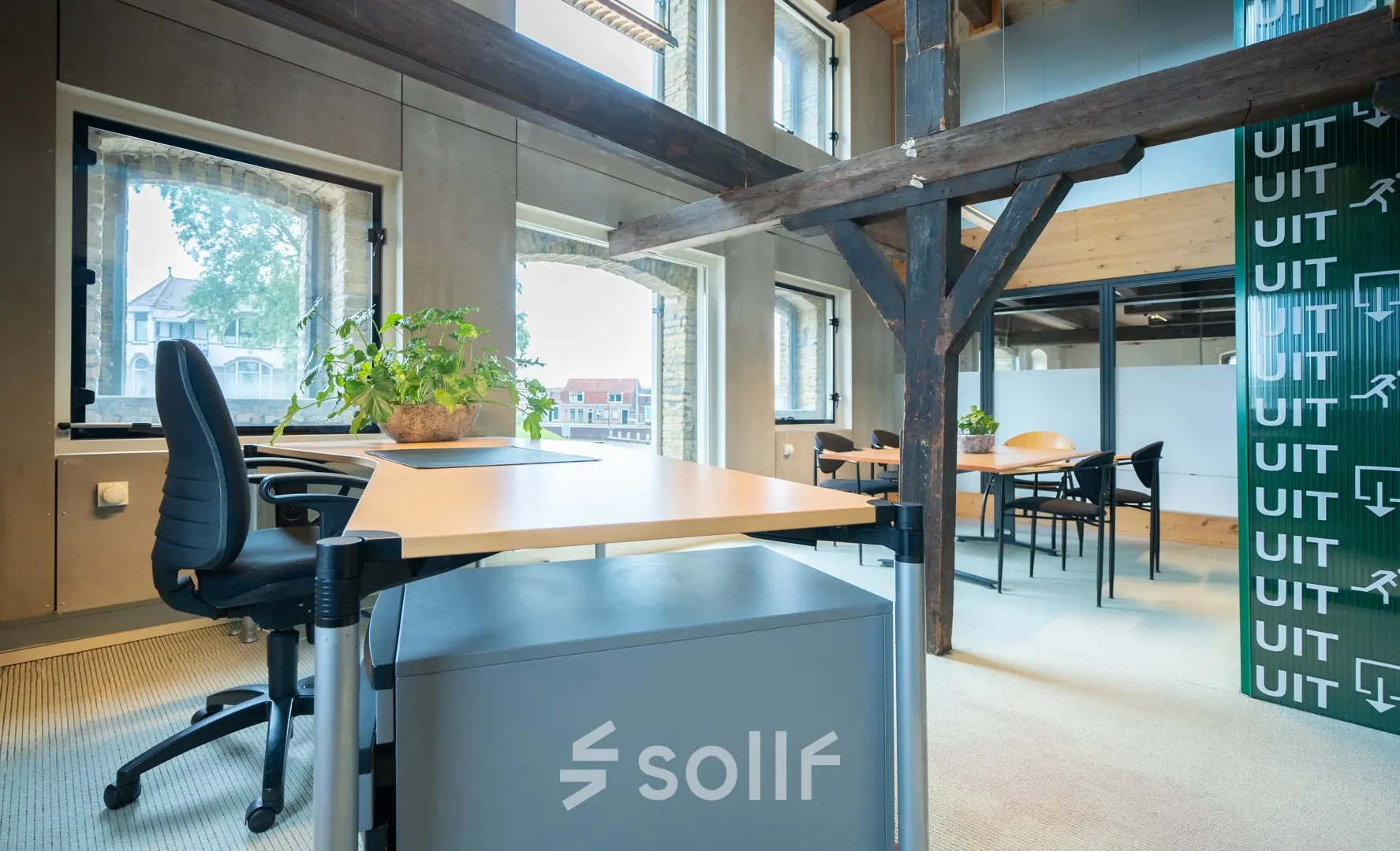 Office space rental at Prins Hendrikkade 3, Franeker, featuring multiple workspaces with desks and chairs, natural light from large windows, and industrial beams.