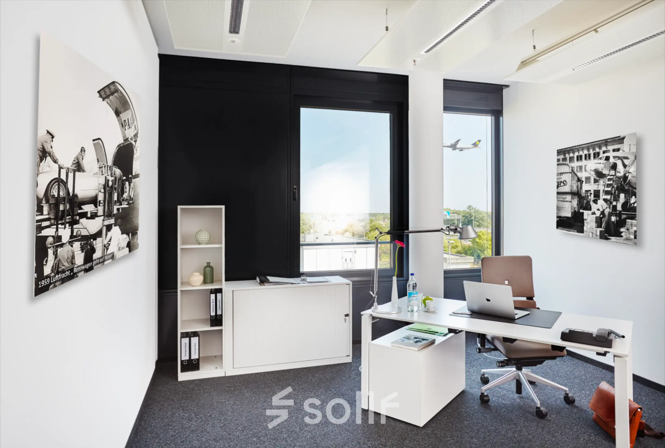 Bright, modern office space with a desk, chair, and shelving unit, showcasing an open window view and airplane art, suitable for rent at Solmsstrasse 83, Frankfurt Bockenheim.