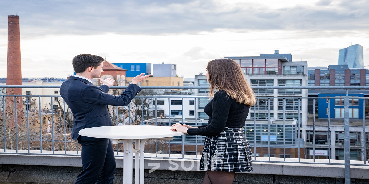 Three people at a rooftop table discussing business with a view of Frankfurt East skyline.