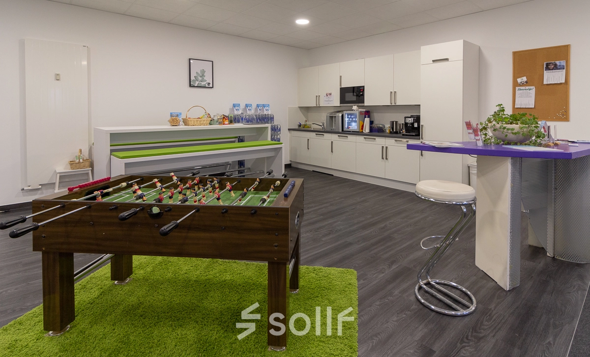 Bright office space featuring a foosball table, kitchenette with white cabinets, and bar seating area located in Frankfurt West, perfect for an office space rental.