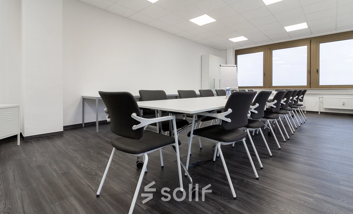 Spacious office to rent in Frankfurt West featuring a bright conference room with tables and chairs, ready for office space rental. Large windows provide natural light.