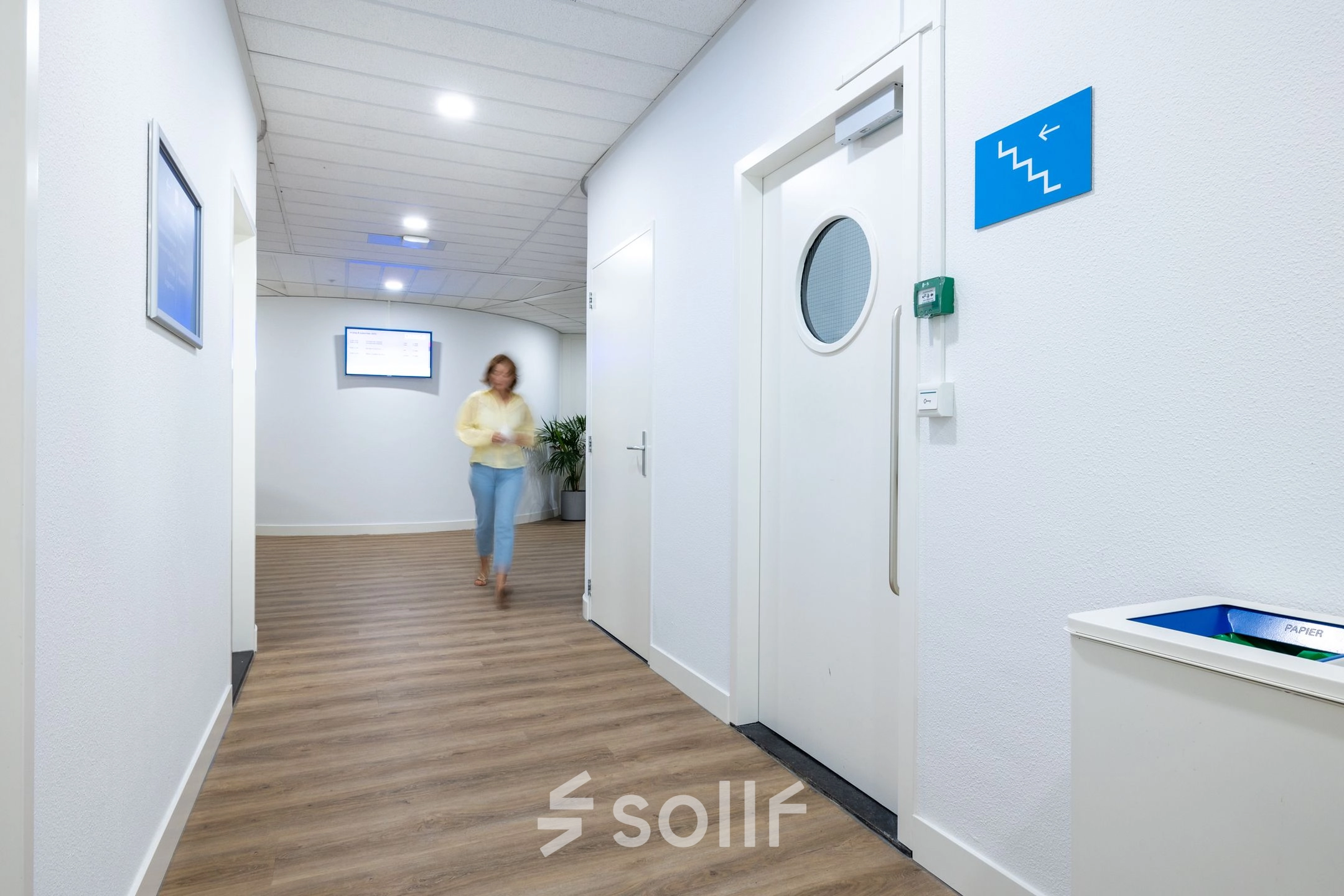 Bright hallway at Groningenweg 8 8, Gouda, suitable for office space rental, with a person walking towards a door, featuring wood-patterned flooring and minimal decor.
