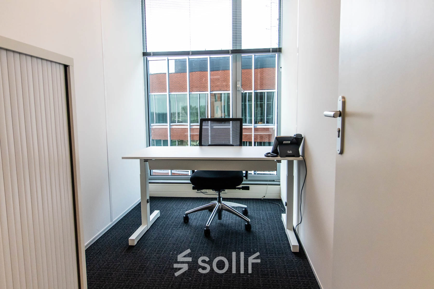 Compact office space for rent at Kampenringweg 45, Gouda, featuring a desk, chair, and a phone with window views.