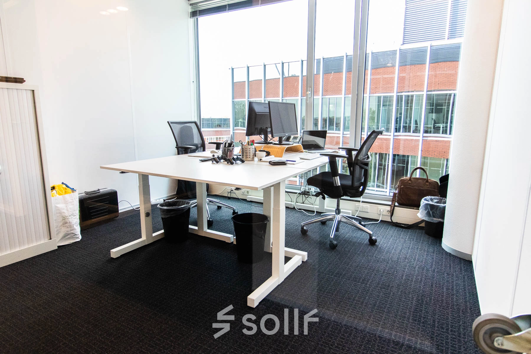 Modern furnished office space for rent at Kampenringweg 45, Gouda, featuring a desk with chairs, computers and office supplies near large windows.